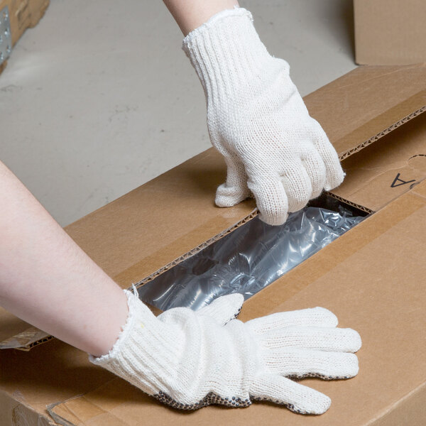 A person wearing Cordova work gloves with black PVC dots opening a box.