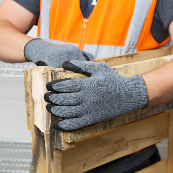 A person wearing Cordova gray warehouse gloves holding a piece of wood.
