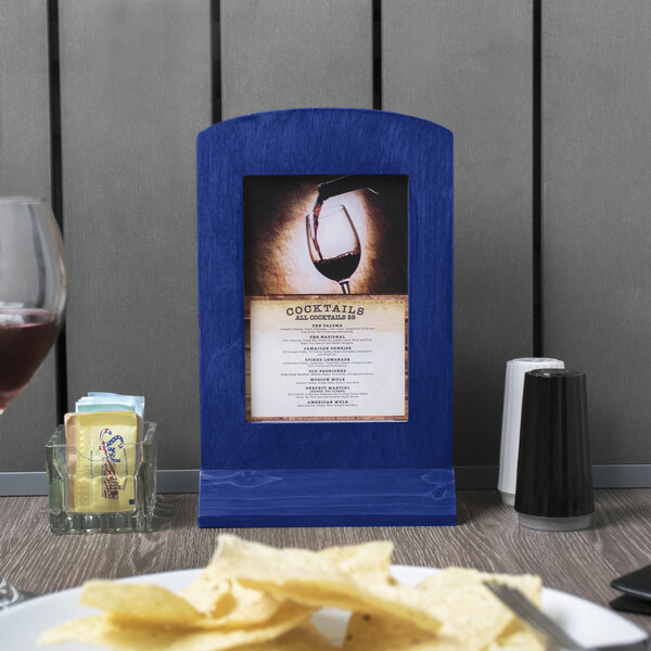 A Menu Solutions True Blue wooden framed menu tent with an angled base on a table.