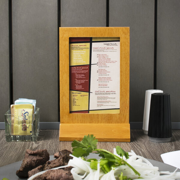 A Menu Solutions Country Oak wood menu tent on a table with a plate of food.