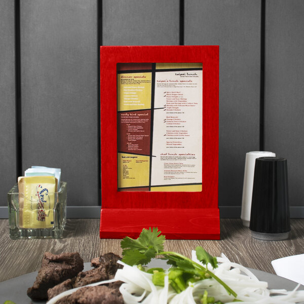 A red framed wood menu tent on a table with a plate of food.