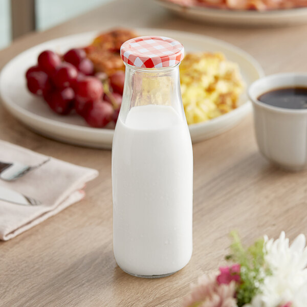 A clear glass milk bottle with a red and white checkered lid, filled with milk.