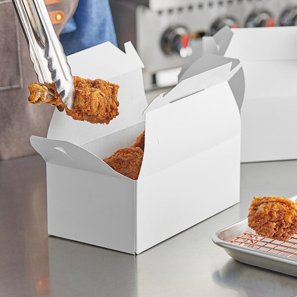 A person holding a pair of fried chicken in a white Barn take out box.