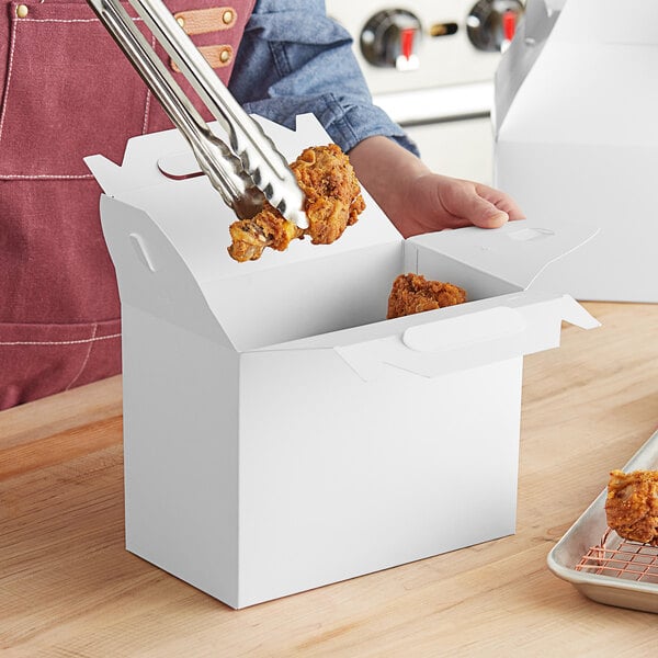 A person holding a white barn take out box with fried chicken inside.