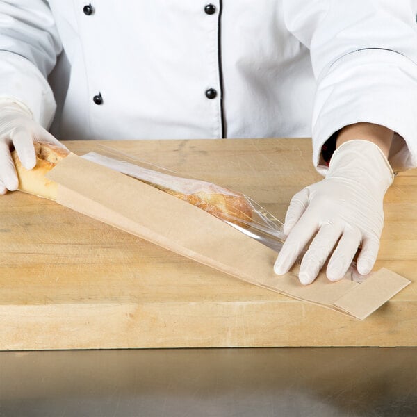 A person in white gloves holding a Bagcraft Packaging Dubl View Kraft Bakery Bag with bread.