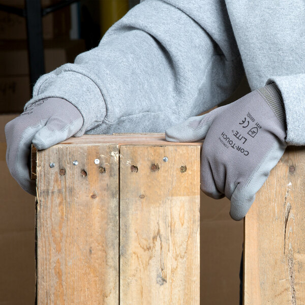 A person wearing Cordova gray nylon gloves with gray polyurethane palm coating holding a piece of wood.