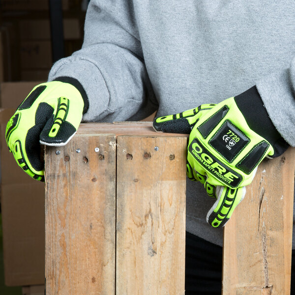 A person wearing lime green Cordova OGRE gloves with yellow accents holding a piece of wood.