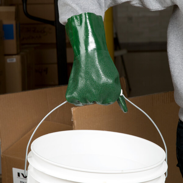 A person wearing green Cordova supported gloves holding a bucket.