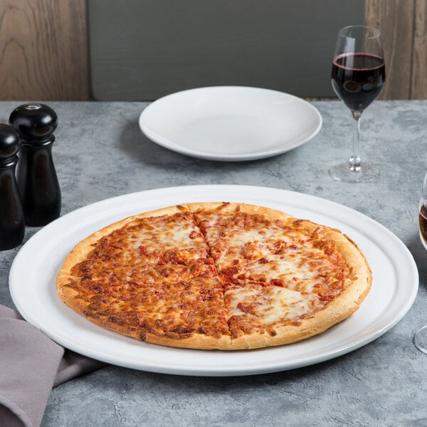 An American Metalcraft white ceramic pizza serving tray with a pizza on it on a table with two glasses of wine.