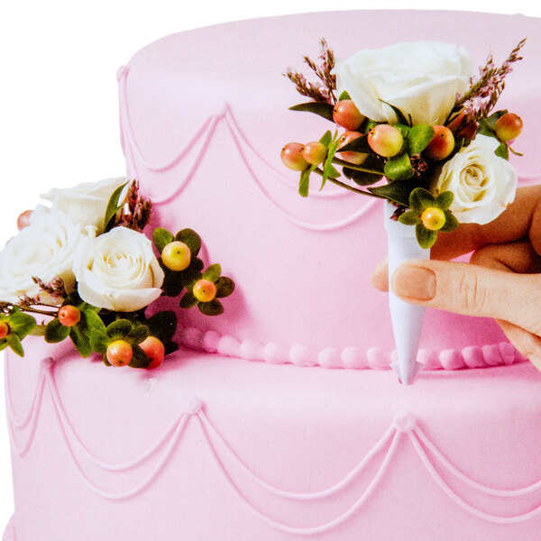A hand holding a Wilton floral cake spike on a pink cake decorated with flower bouquet.
