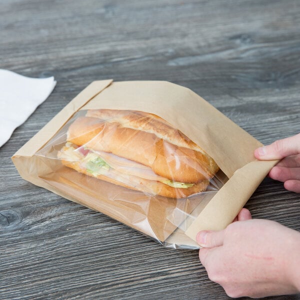 A person opening a Bagcraft Packaging Dubl View ToGo! Kraft paper bag with a sandwich inside.
