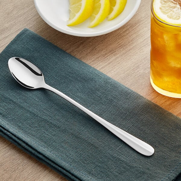 An Acopa Benson iced tea spoon on a napkin next to a lemon slice and a glass of lemonade.