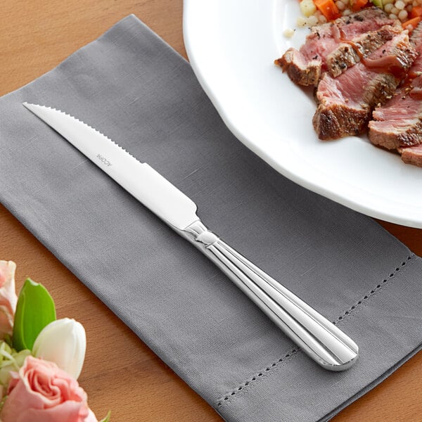 An Acopa Harmony steak knife on a napkin next to a plate of meat.