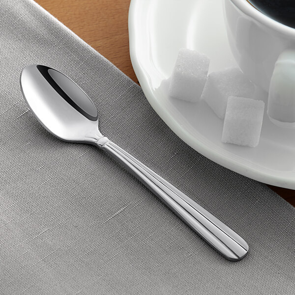 An Acopa stainless steel demitasse spoon on a napkin next to a plate of sugar cubes and a cup of coffee.