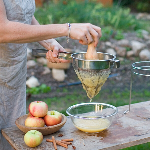 A person using a Weston stainless steel sieve to strain apple juice from a bowl of apples.