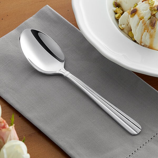 An Acopa stainless steel oval bowl dessert spoon on a napkin next to a bowl of ice cream.