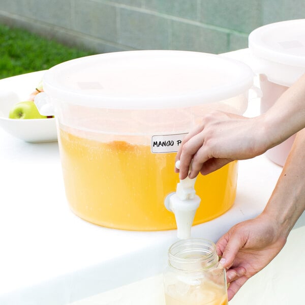A hand pressing a tap into a Choice clear round beverage dispenser filled with orange juice.