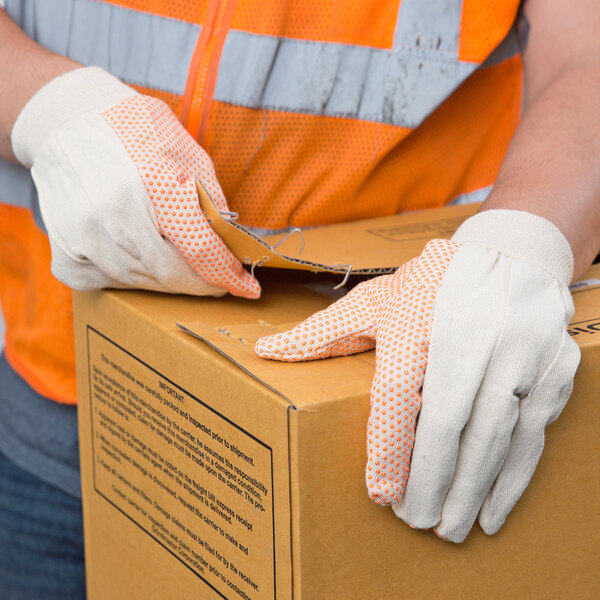 A person wearing Cordova orange safety gloves holding a box.