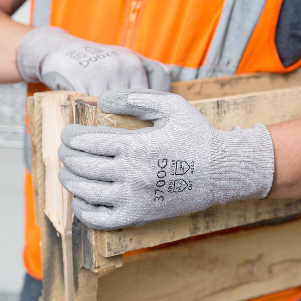 A person wearing Cordova HPPE gloves with gray polyurethane palm coating holding a piece of wood.