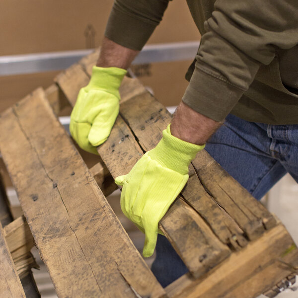 A man wearing Cordova Hi-Vis yellow work gloves holding a wooden pallet.