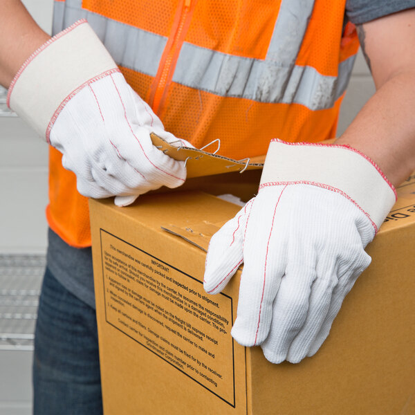A person wearing Cordova Natural Nap-In Polyester / Cotton Work Gloves holding a box.