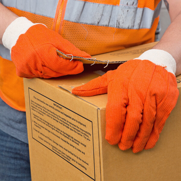 A person wearing Cordova Hi-Vis orange work gloves holding a box.