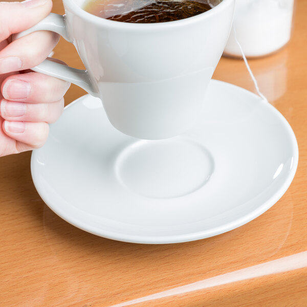 A hand pouring tea into a Tuxton Florence saucer on a white background.