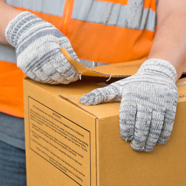 A person wearing Cordova multi-color work gloves holding a box.