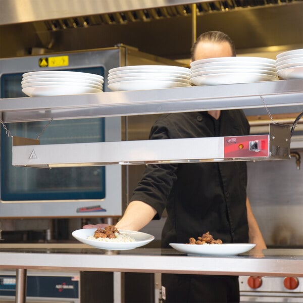 A chef using an Avantco strip warmer to heat a plate of food.