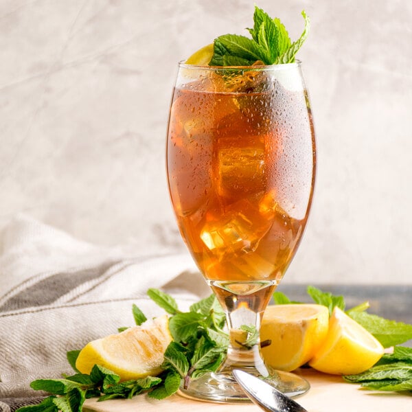 A glass of Narvon unsweetened iced tea with mint leaves and a lemon wedge on a table.