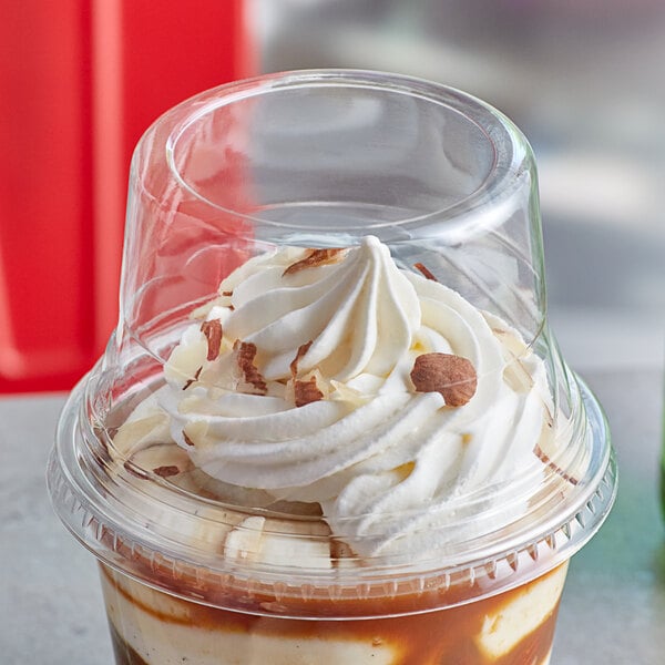 A clear plastic dome lid on a cup of ice cream with whipped cream.