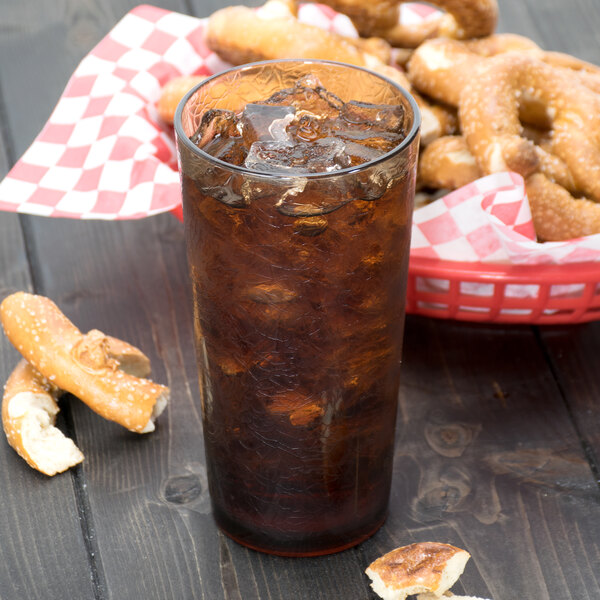 A light amber Cambro plastic tumbler filled with brown liquid and ice on a table with a basket of pretzels.
