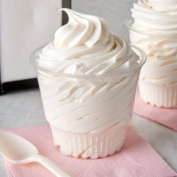 A close-up of two clear plastic dessert cups filled with frozen yogurt, topped with whipped cream and a spoon.