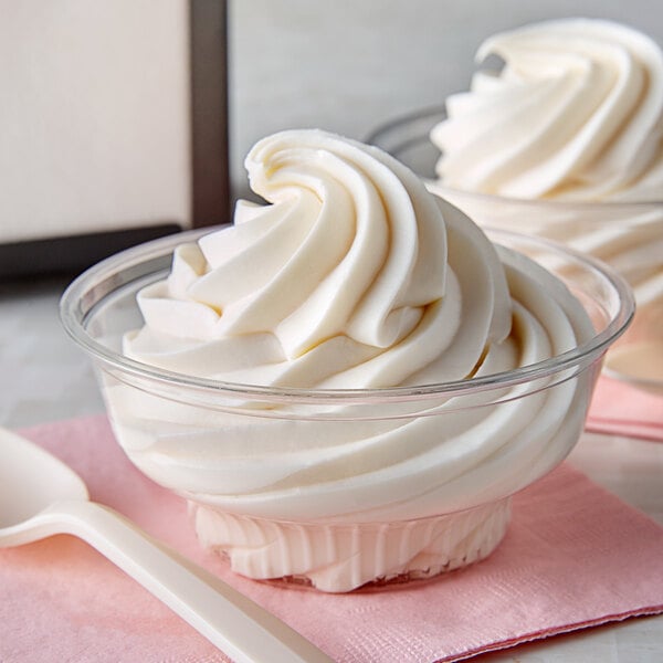 A clear plastic dessert cup filled with soft serve ice cream and frozen yogurt topped with whipped cream and a spoon.