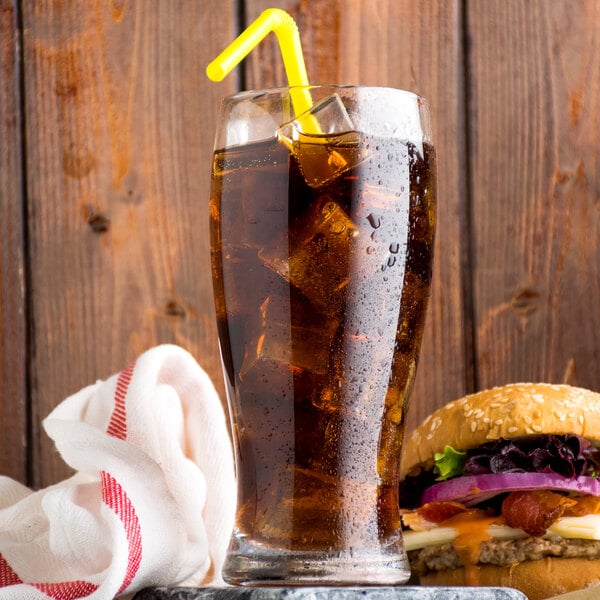 A glass of Narvon Diet Cola with ice and a straw next to a burger on a wooden table.