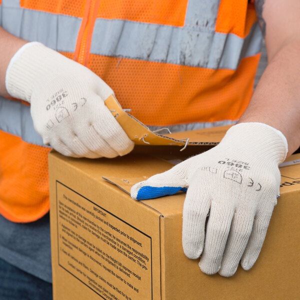A person wearing Cordova Natural Cotton Work Gloves with blue nitrile palm coating holding a box.