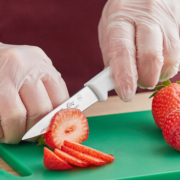A person using a Choice paring knife to cut a strawberry on a green cutting board.