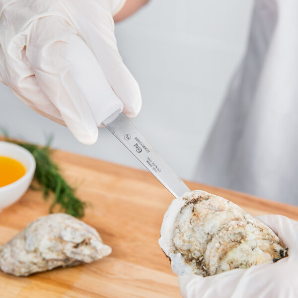 A person in gloves using a Choice Boston Style Oyster Knife to cut an oyster on a counter.