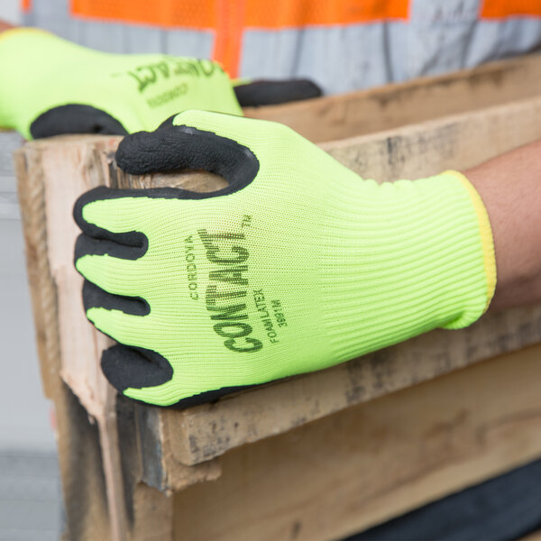 A person wearing Cordova Contact Hi-Vis nylon gloves with black foam latex palm coating holding a wooden pallet.