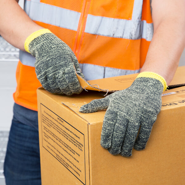 A person wearing Cordova Power-Cor Max Camo cut resistant gloves and a safety vest is holding a box.