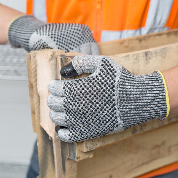 A person wearing Cordova Monarch gray and white dotted work gloves holding a piece of wood.