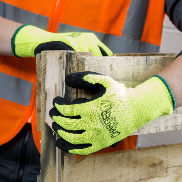 A person wearing Cordova Hi-Vis green safety gloves holding a piece of wood.
