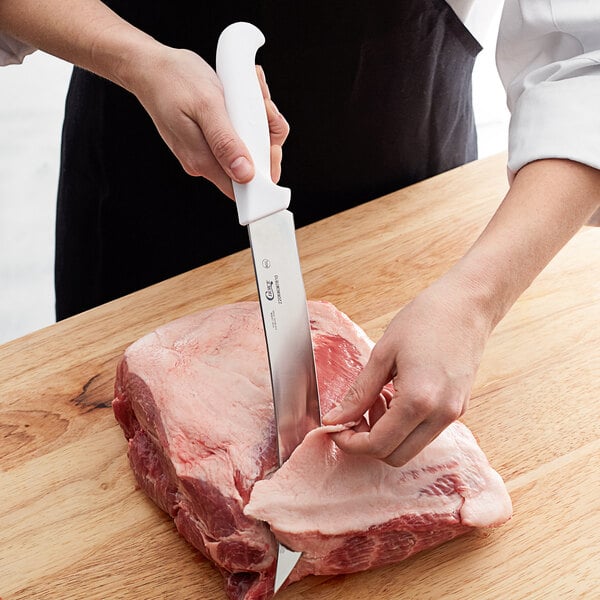 A person cutting meat with a Choice 10" Cimeter Knife on a wooden surface.