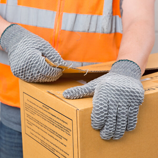 A person wearing Cordova gray warehouse gloves holding a box.