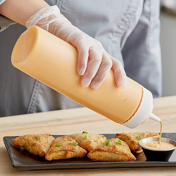 A person using a Choice clear wide mouth squeeze bottle to pour sauce on a plate of fried food.