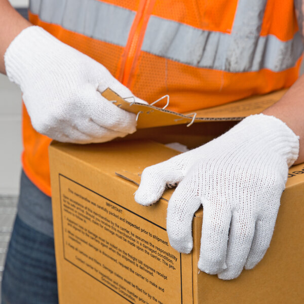 A person wearing Cordova white polyester/cotton work gloves with black PVC dots on the palm opening a box.