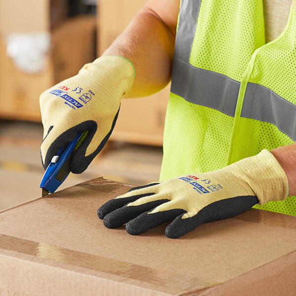 A person wearing Cordova ActivGrip Advance Kevlar gloves and a safety vest holding a box.