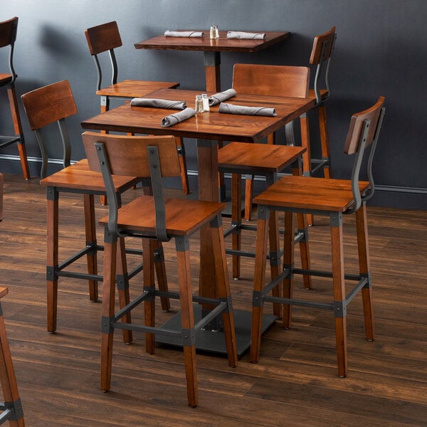 A Lancaster Table & Seating square wooden bar height table with a brown live edge surface and metal legs.