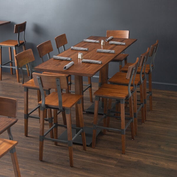 A Lancaster Table & Seating solid wood live edge bar height table with chairs and napkins on it.