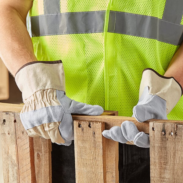A man wearing Cordova canvas work gloves and a safety vest holding a piece of wood.